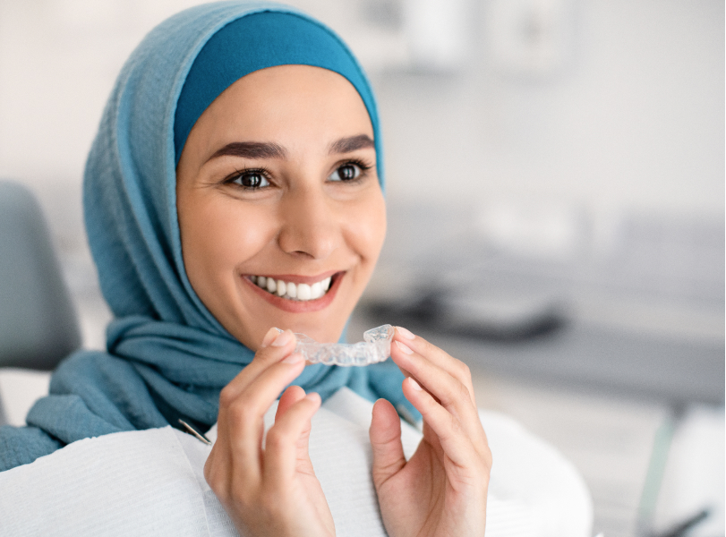 A young woman holding a clear aligner tray and smiling confidently, showing the feeling that VCCID aims to provide its patients with through clear aligner treatment and Invisalign in Burnaby