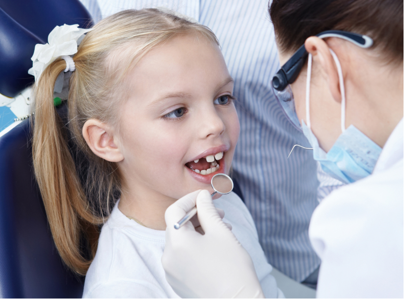 A dentist gently examining a contented child's teeth, illustrating the positive experience that young patients receive when visiting VCCID in Burnaby for children's dentistry