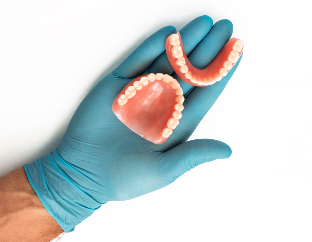 A gloved hand holding a set of full dentures like those available at VCCID in Burnaby